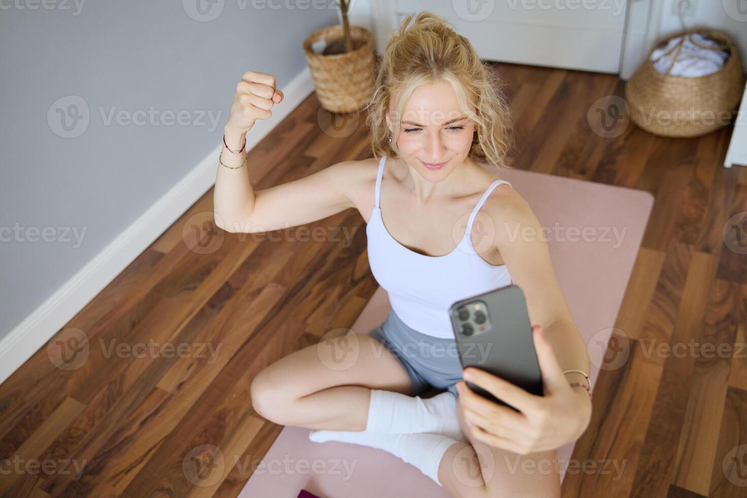 ung sportig kondition tränare, yoga instruktör gör leva ström, tar selfies på smartphone medan Sammanträde på sudd matta på Hem, inspelning henne träna Träning session foto