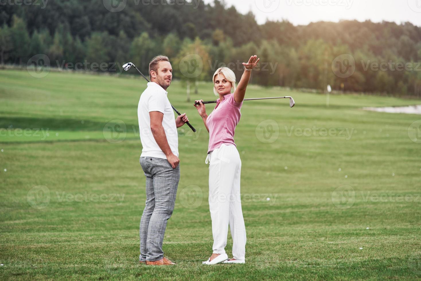 räcker upp handen för att visa nästa destination. par golfspelare med pinnar stående på gräsmattan foto