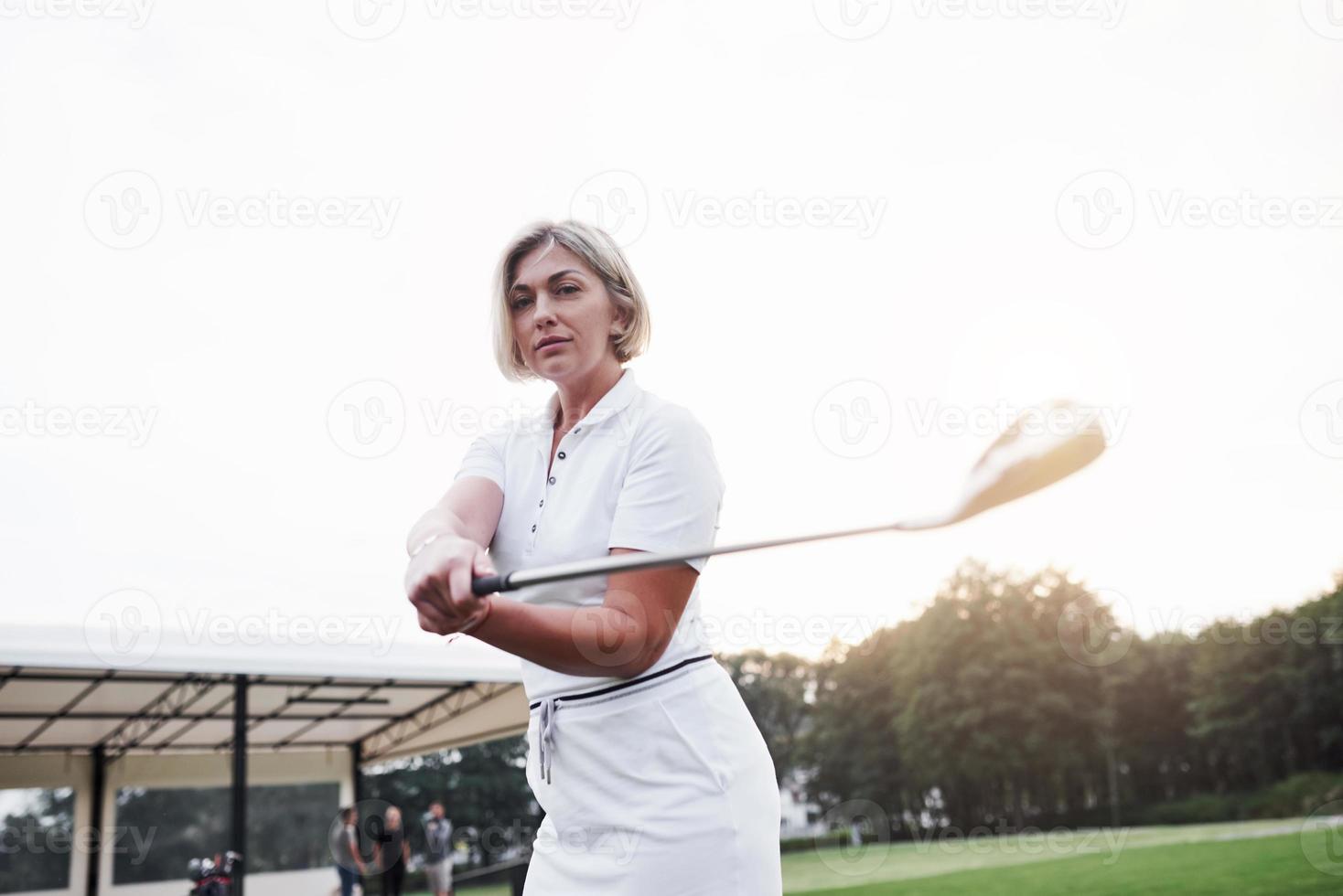 foto av vacker blond vuxen kvinna som håller golfpinne på det gröna sportfältet