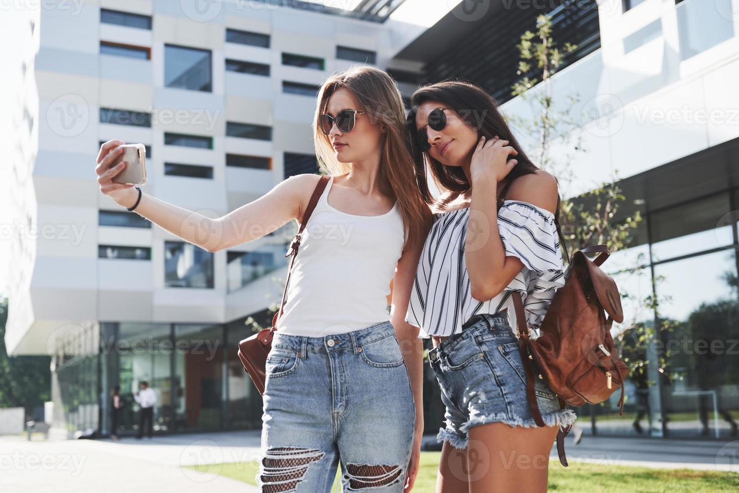 två vackra glada unga student flicka med ryggsäck nära universitetets campus och göra selfie foto. utbildning och fritid koncept foto