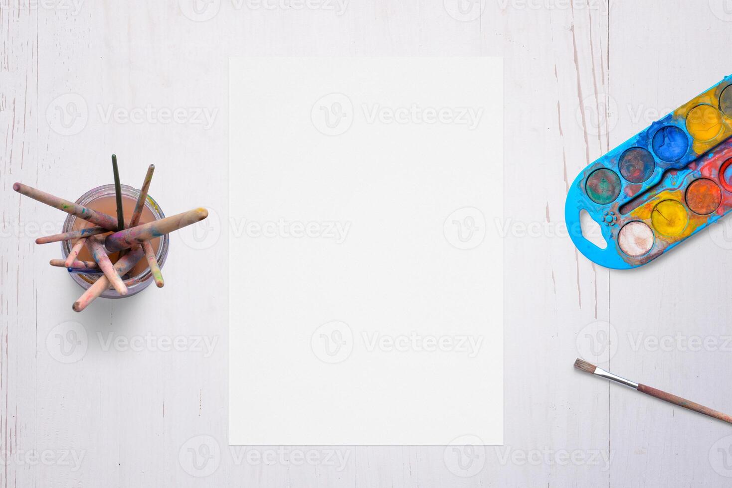 tom vit papper på skrivbord, omgiven förbi borstar och vattenfärger. idealisk för konstnärlig kreativitet, målning koncept, eller design teman. foto