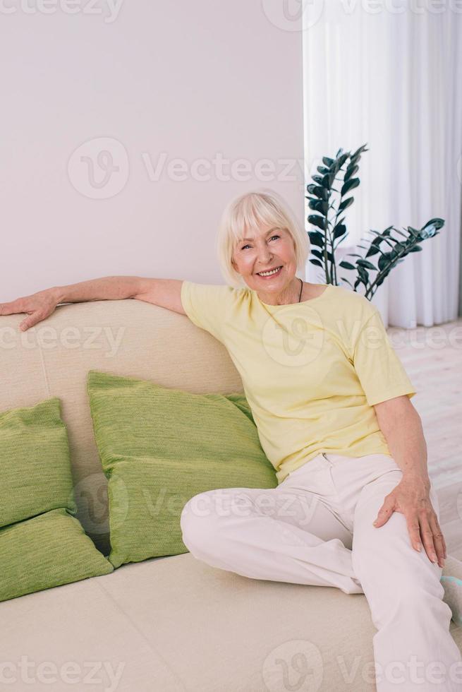 glada kaukasiska snygg kvinna med grått hår sitter i soffan hemma. anti age, hälsosam livsstil, positivt tänkande koncept foto