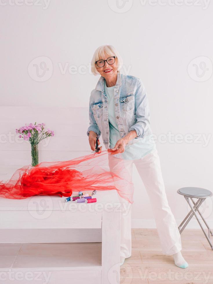 senior pensionär glad snygg kvinna kläddesigner i jeansjacka på jobbet. handgjorda, mode, hobby, design, ålder koncept foto