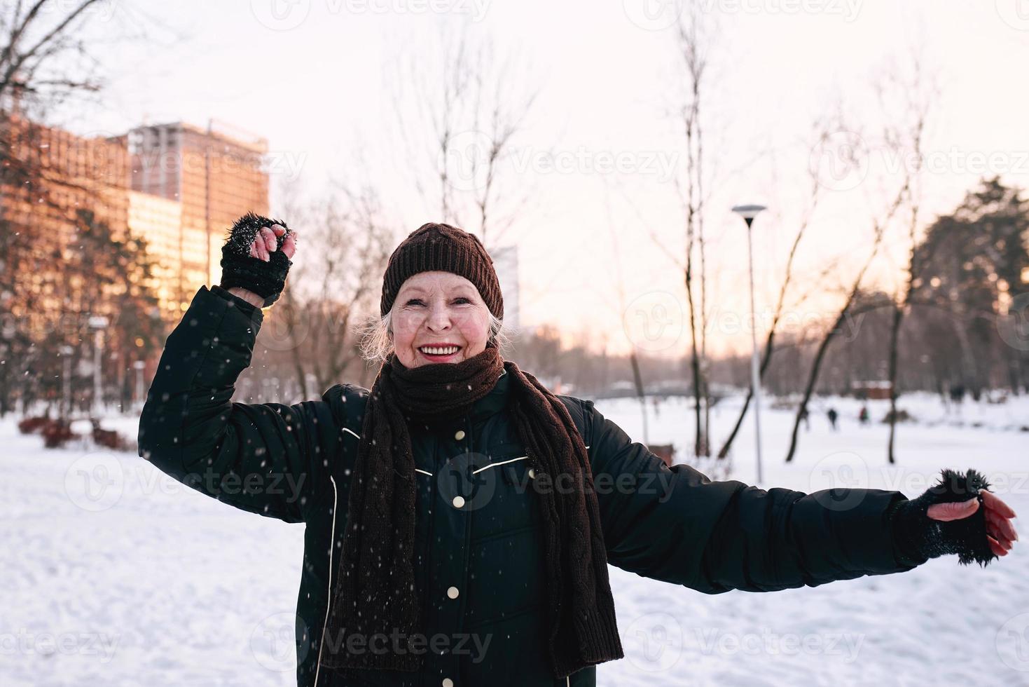 senior kvinna i hatt och sportig jacka gör sportövningar i snö vinterpark. vinter, ålder, sport, aktivitet, säsong koncept foto