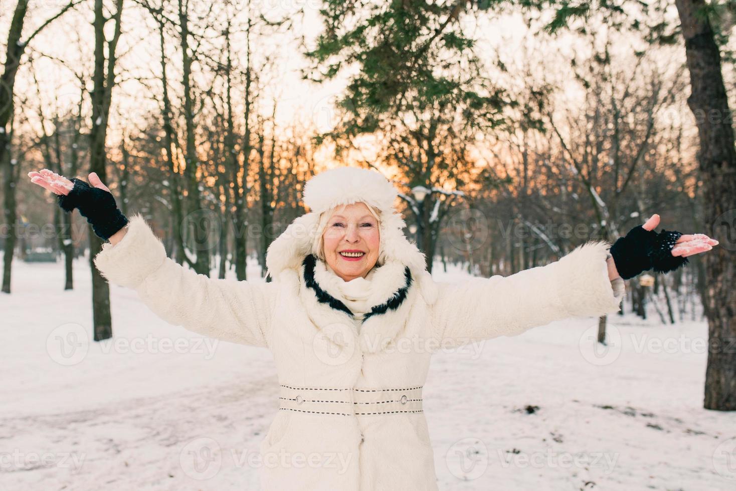 senior kvinna i vit hatt och päls njuter av vintern i snöskog. vinter, ålder, säsong koncept foto
