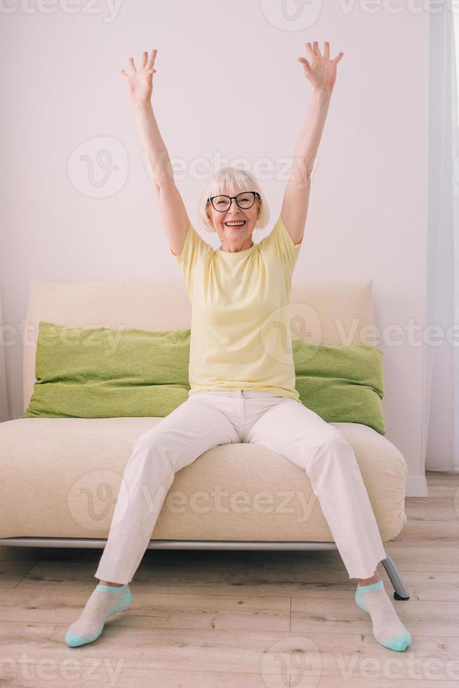 glada kaukasiska snygg kvinna med grått hår sitter i soffan hemma. anti age, hälsosam livsstil, positivt tänkande koncept foto