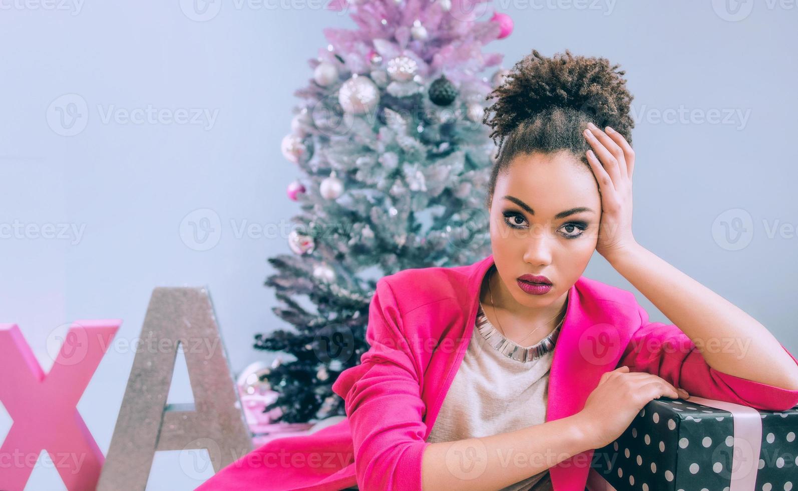 ledsen afroamerikansk kvinna vid julgranen besviken över julklappen. jul, nyår, frustration, lycka, semester koncept foto