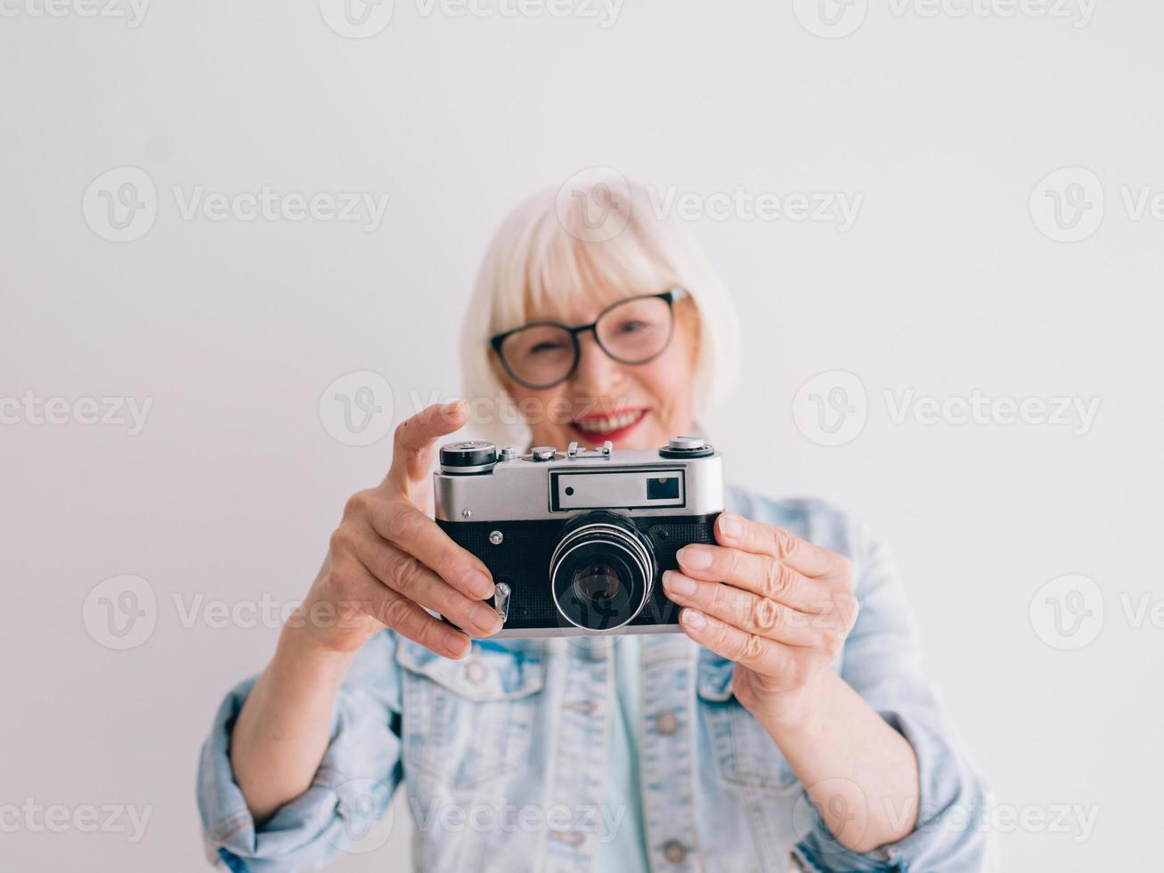 senior snygg kvinna med grått hår och i glasögon och jeansjacka tar bilder av blommor med filmkamera. ålder, hobby, anti age, positiva vibbar, fotografi koncept foto