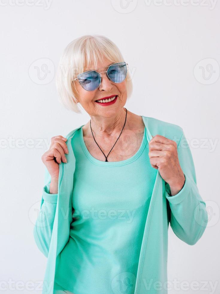 senior snygg glad kvinna i blå solglasögon och turkosa kläder. sommar, resor, anti ålder, glädje, pension, frihet koncept foto