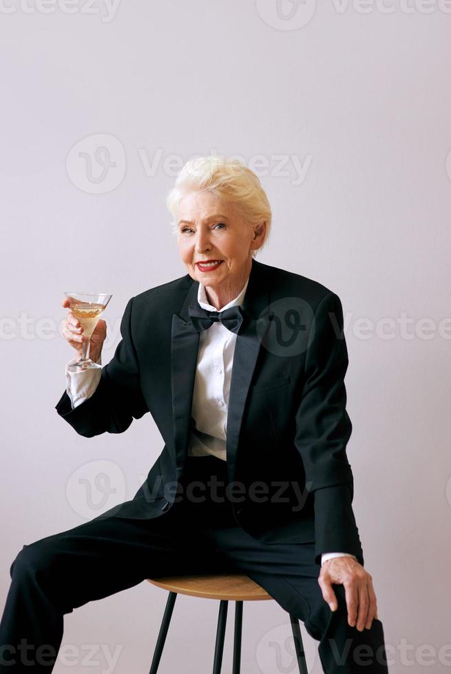 snygg mogen sommelier senior kvinna i smoking med ett glas vin. kul, fest, stil, livsstil, arbete, alkohol, firande koncept foto