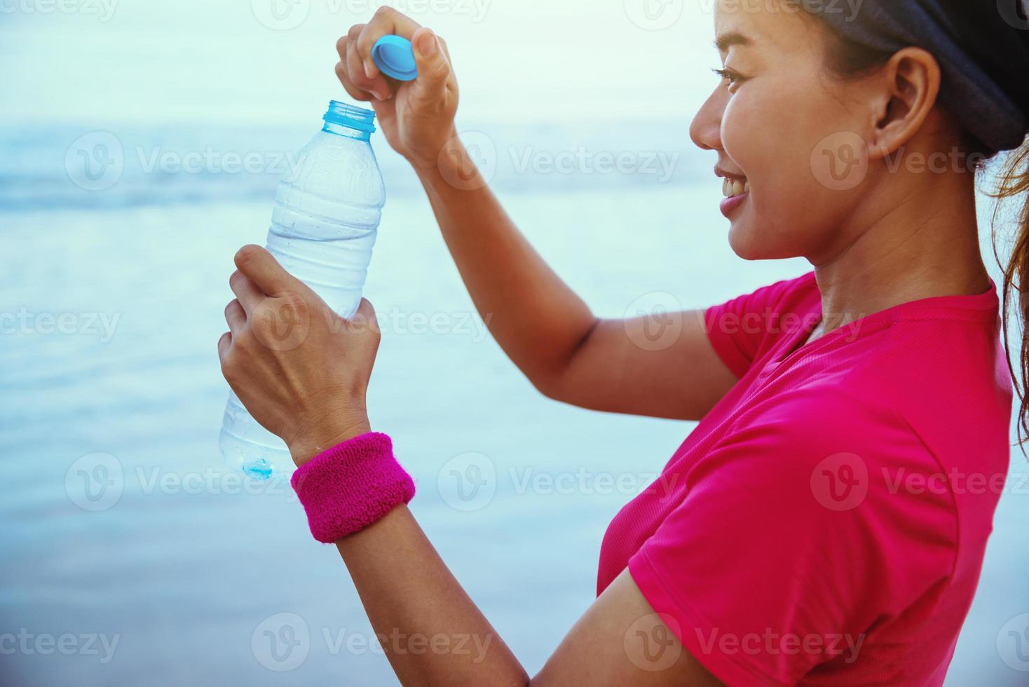 asiatiska kvinnor jogging träning på stranden på morgonen. koppla av med havspromenaden och dricksvatten från plastflaskorna foto