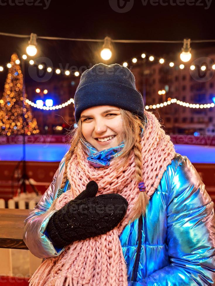 glada leende ung kaukasisk kvinna i halsduk, mössa, jacka, vantar vid utomhusbanan. nytt år, roligt, vinterkoncept foto