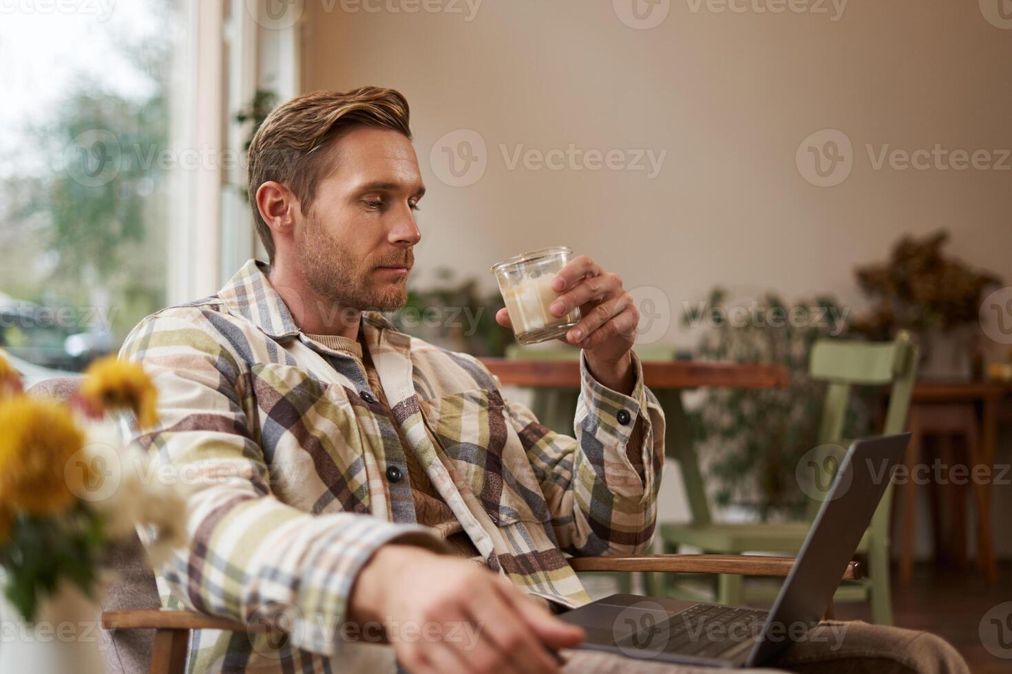 porträtt av ung frilansare, en man i tillfällig kläder, Sammanträde i Kafé och dricka kaffe, arbetssätt avlägset på bärbar dator, digital nomad håller på med hans projekt utomhus i sam-arbetande Plats foto
