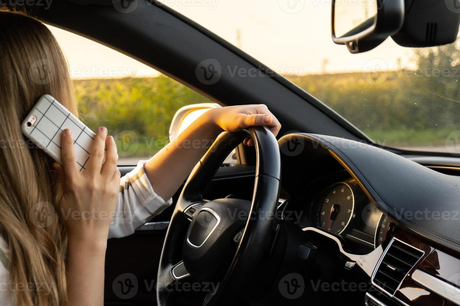 ung kvinna använder sig av mobil telefon medan körning bil på motorväg väg under solnedgång. kvinnoförare har olycka kallelse med smartphone för hjälp. företag kvinna upptagen körning begrepp foto