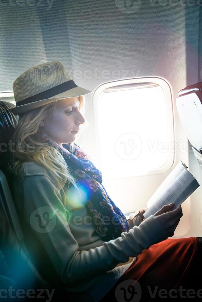 ung kaukasisk turist kvinna ensam läsa en bok inuti flygplan foto