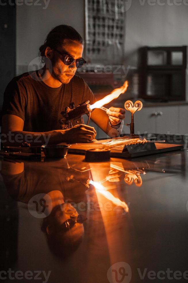glasblåsande ung man som arbetar på en facklaslåga med glasrör foto
