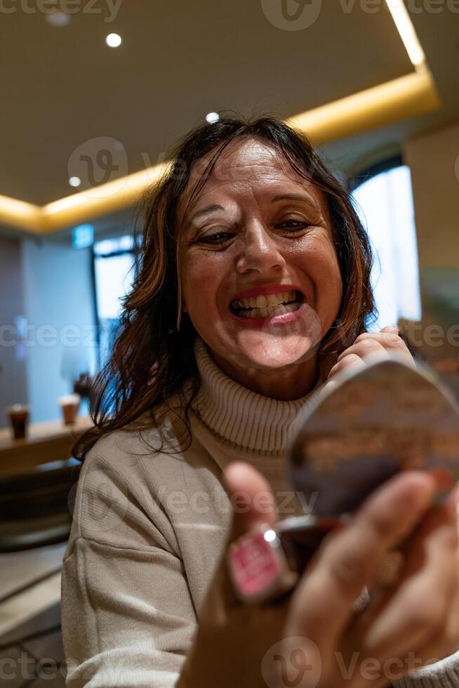 skön mogna turist kvinna sätta läppstift Sammanträde i en Kafé på en ha sönder foto