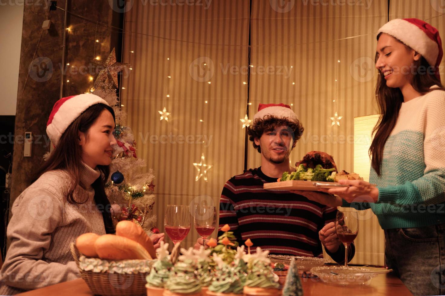 en familjs speciella måltid, ung hona serverar rostad kalkon till vänner och glad med drinkar under en middag hemma i matsalen dekorerad för julfest och nyårsfest. foto