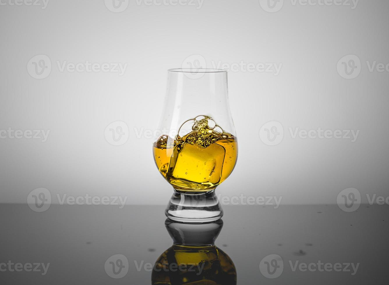 provsmakningsglas med en dram skotsk whisky och isbit som faller ner i det. foto