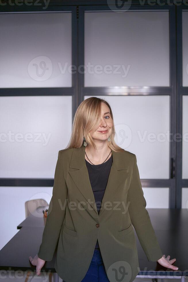 blond kvinna med lång hår i en grön jacka och jeans i de kontor foto