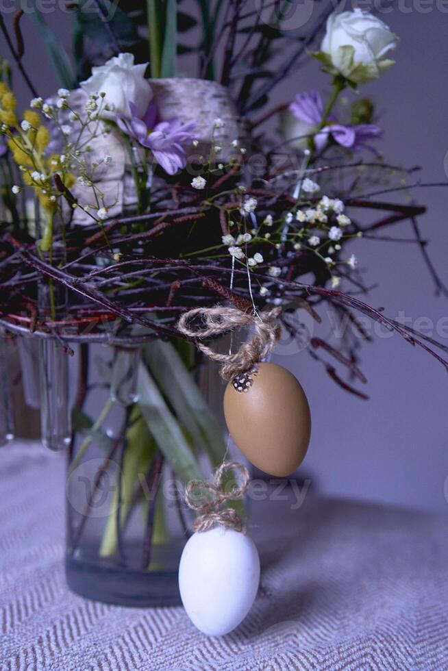 påsk krans, bo av vide grenar och blommor dekorerad med ägg och glas testa rör i en transparent vas foto