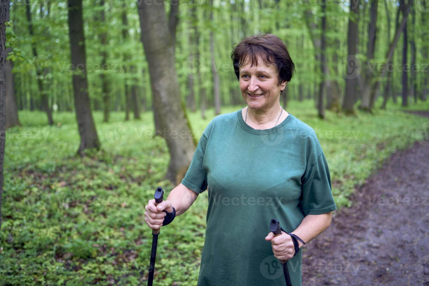 äldre kvinna är engagerad i nordic gående med pinnar i de vår skog foto