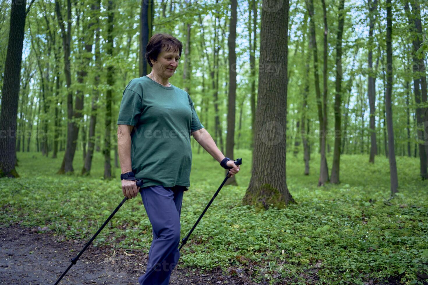 äldre kvinna är engagerad i nordic gående med pinnar i de vår skog foto