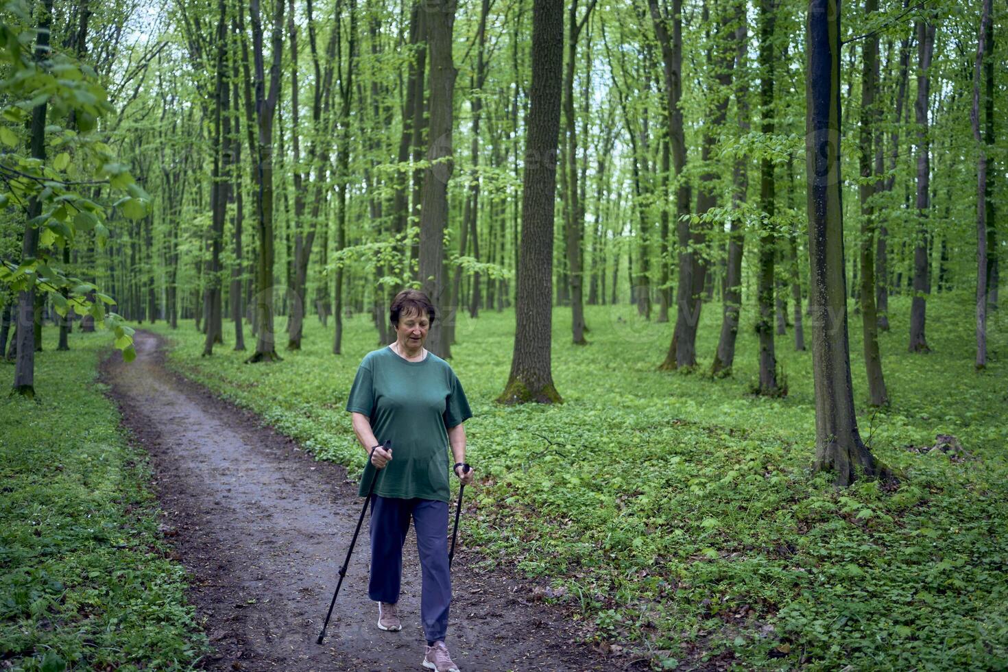 äldre kvinna är engagerad i nordic gående med pinnar i de vår skog foto