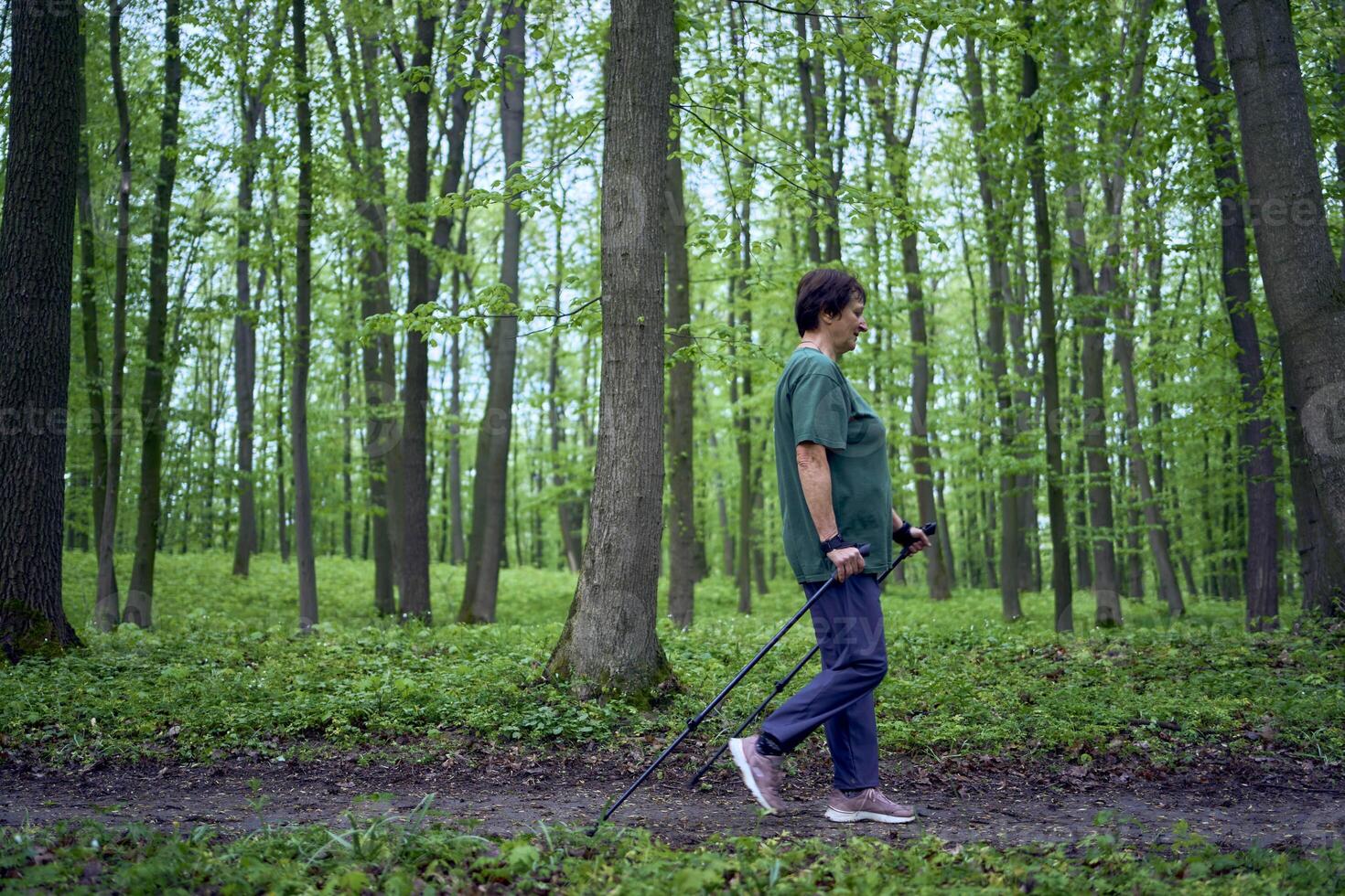 äldre kvinna är engagerad i nordic gående med pinnar i de vår skog foto