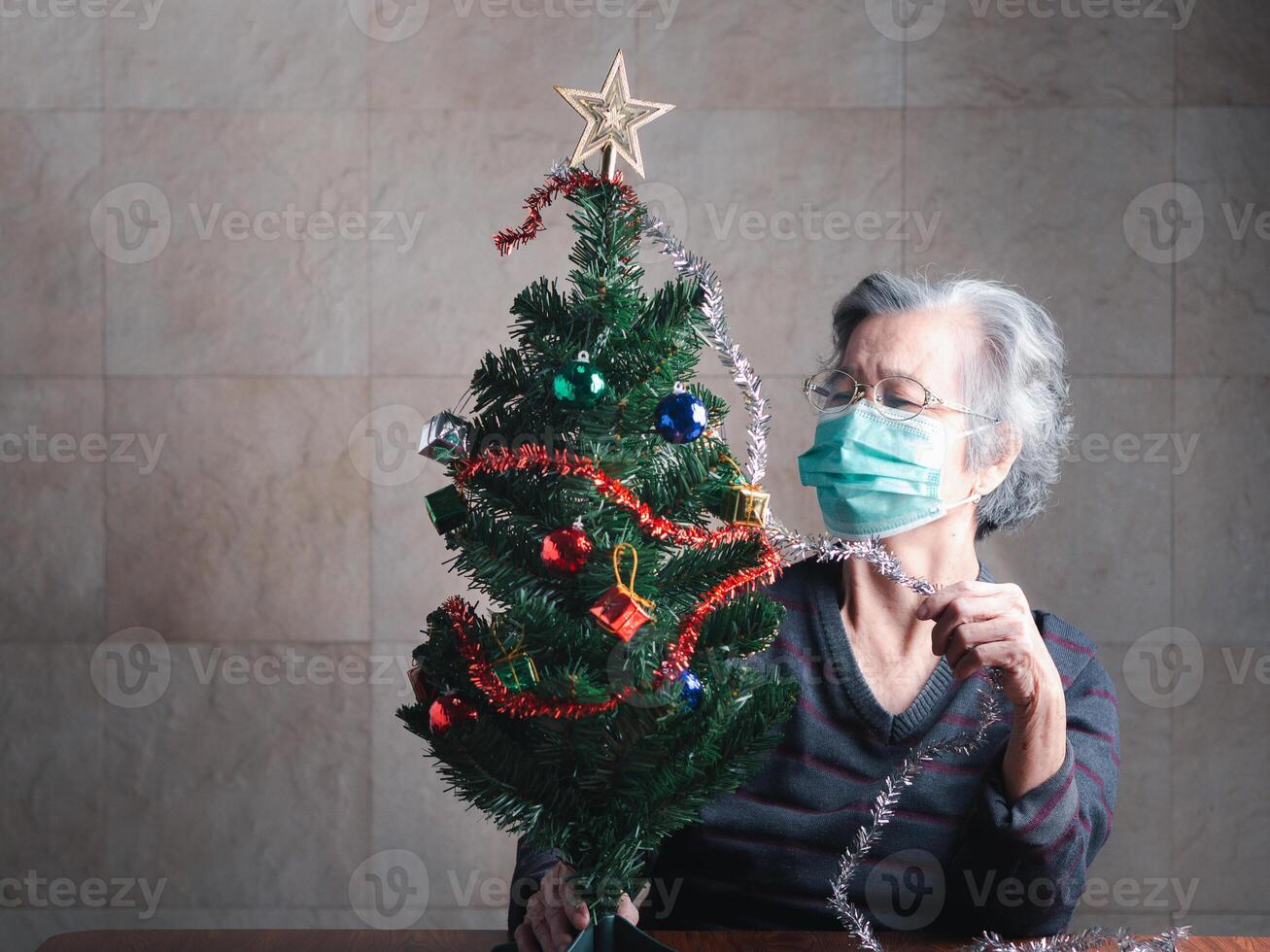 äldre asiatisk kvinna bär en mask och dekorera de jul träd medan Sammanträde i en levande rum på Hem. begrepp av åldrig människor, sjukvård och jul, och Lycklig ny år festival foto