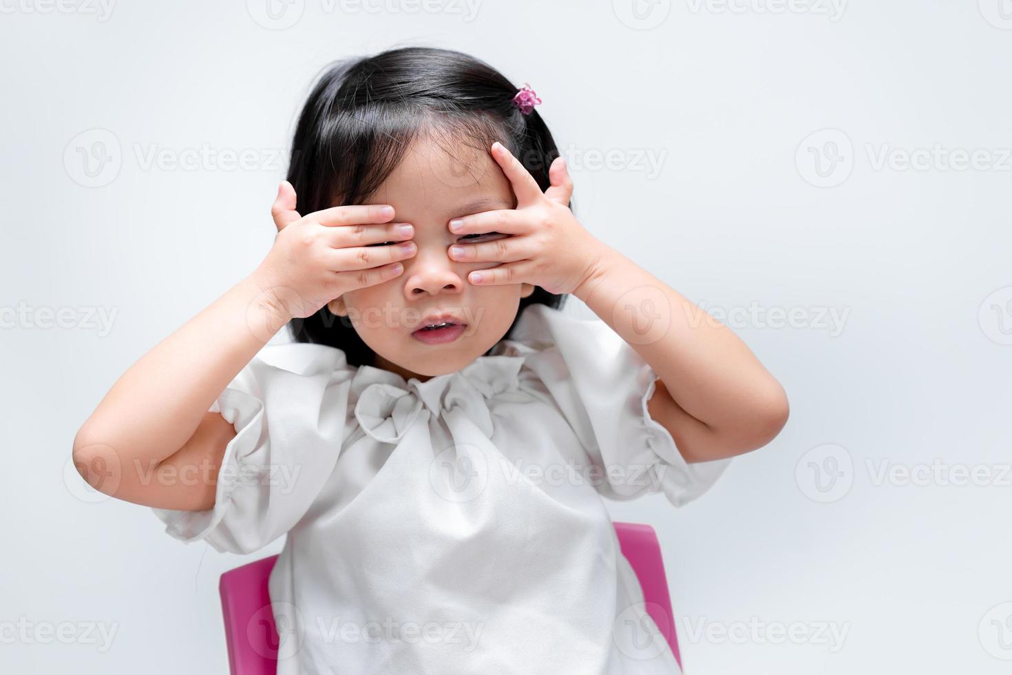 liten barn flicka tittar genom hennes hand med ena ögat. på isolerade vit bakgrund. förskola i åldern 4-5 år. foto