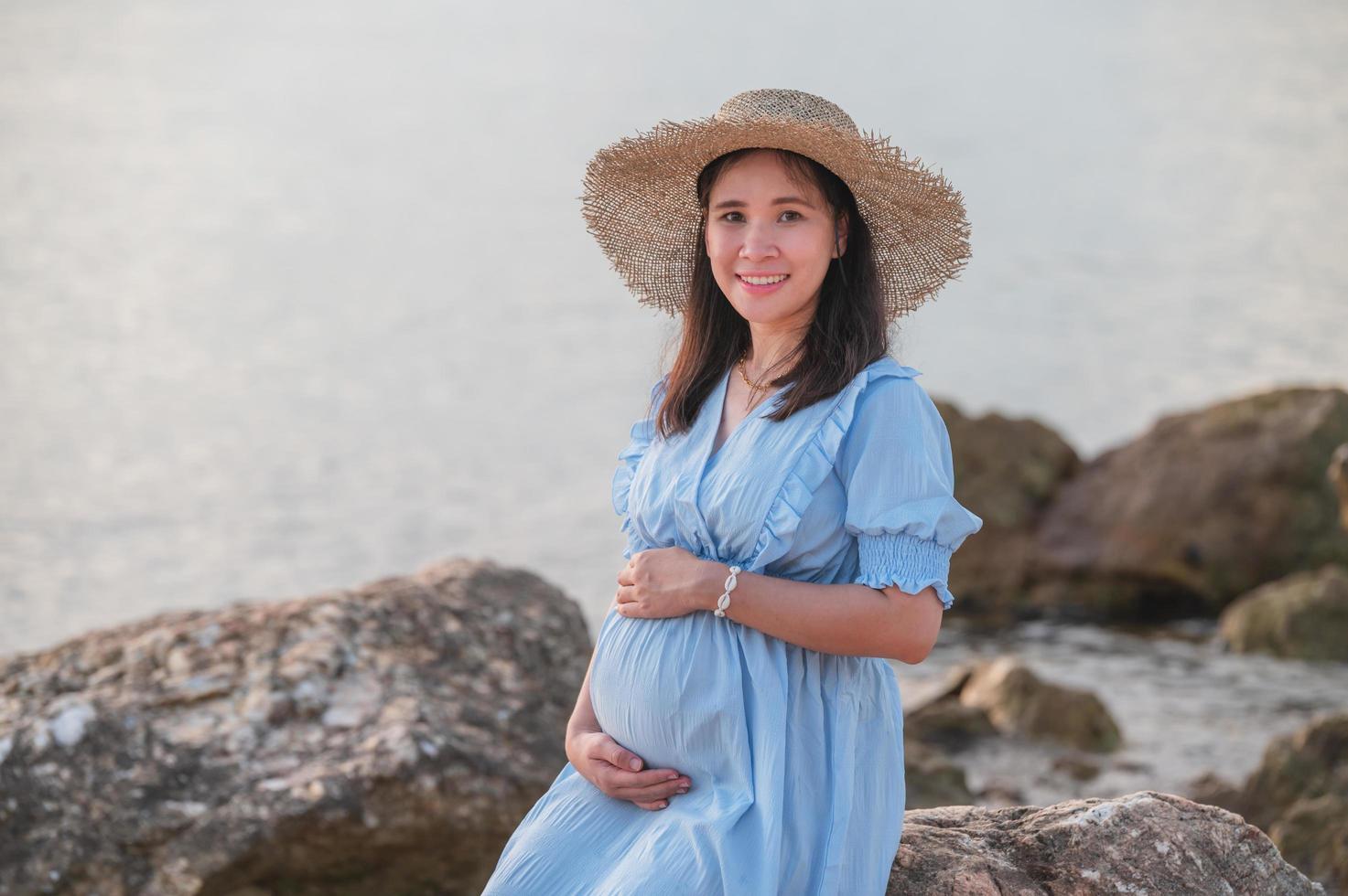 gravid kvinna sitter på klipporna nära sandstranden och havet. foto