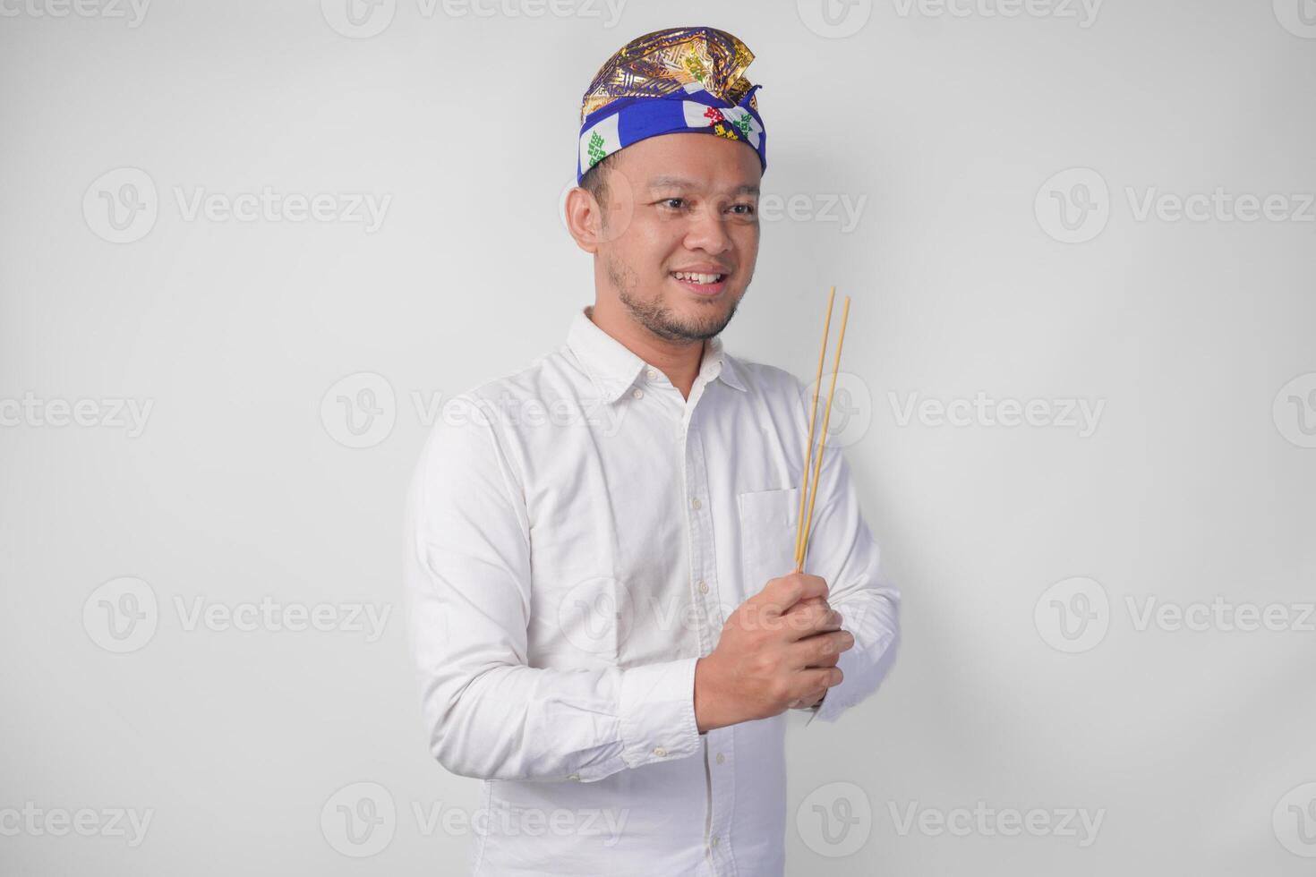 balinesisk man bär traditionell huvudbonad kallad udeng håller på med betalande respekt gest medan innehav bön- rökelse på isolerat vit bakgrund foto
