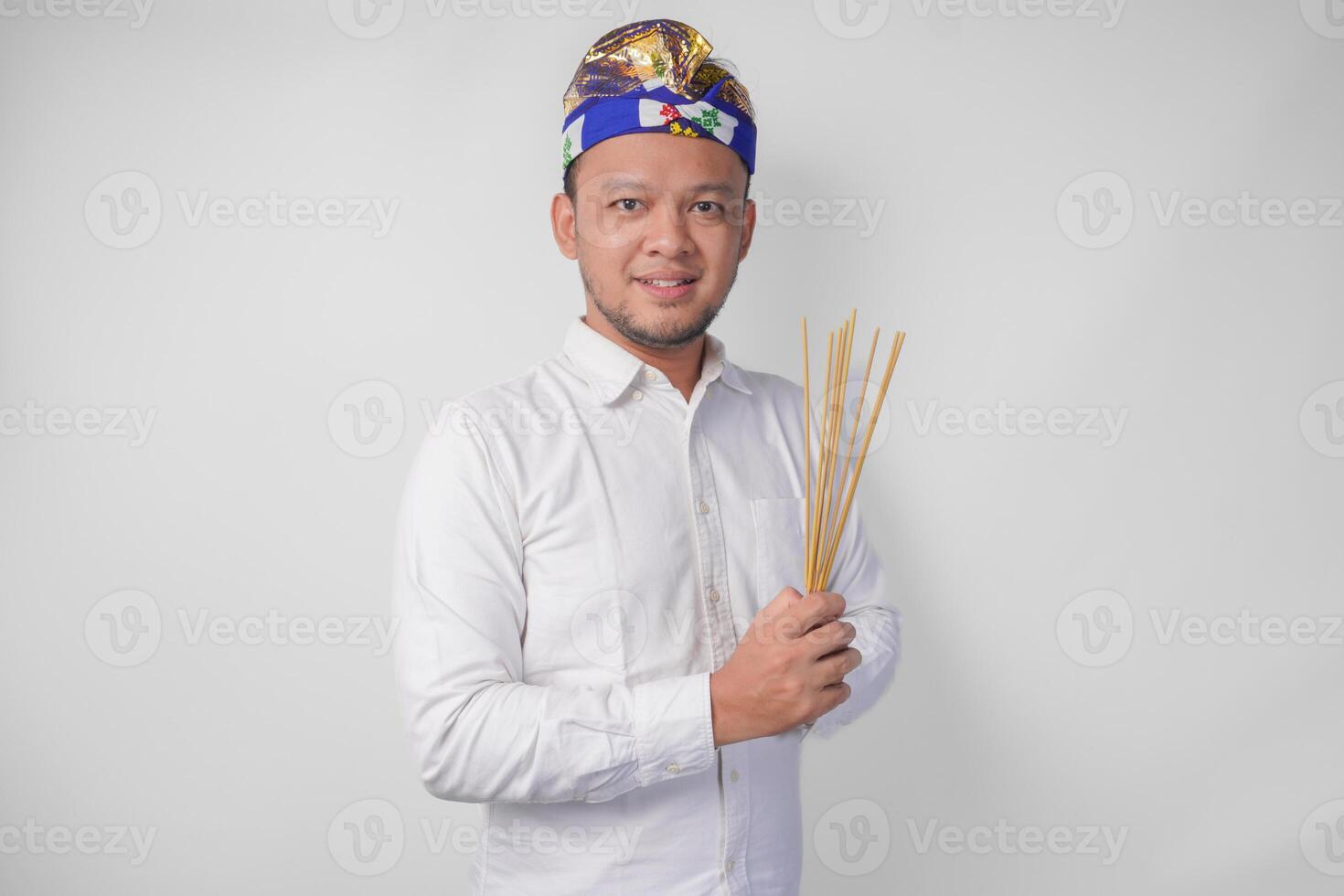 balinesisk man bär traditionell huvudbonad kallad udeng håller på med betalande respekt gest medan innehav bön- rökelse på isolerat vit bakgrund foto