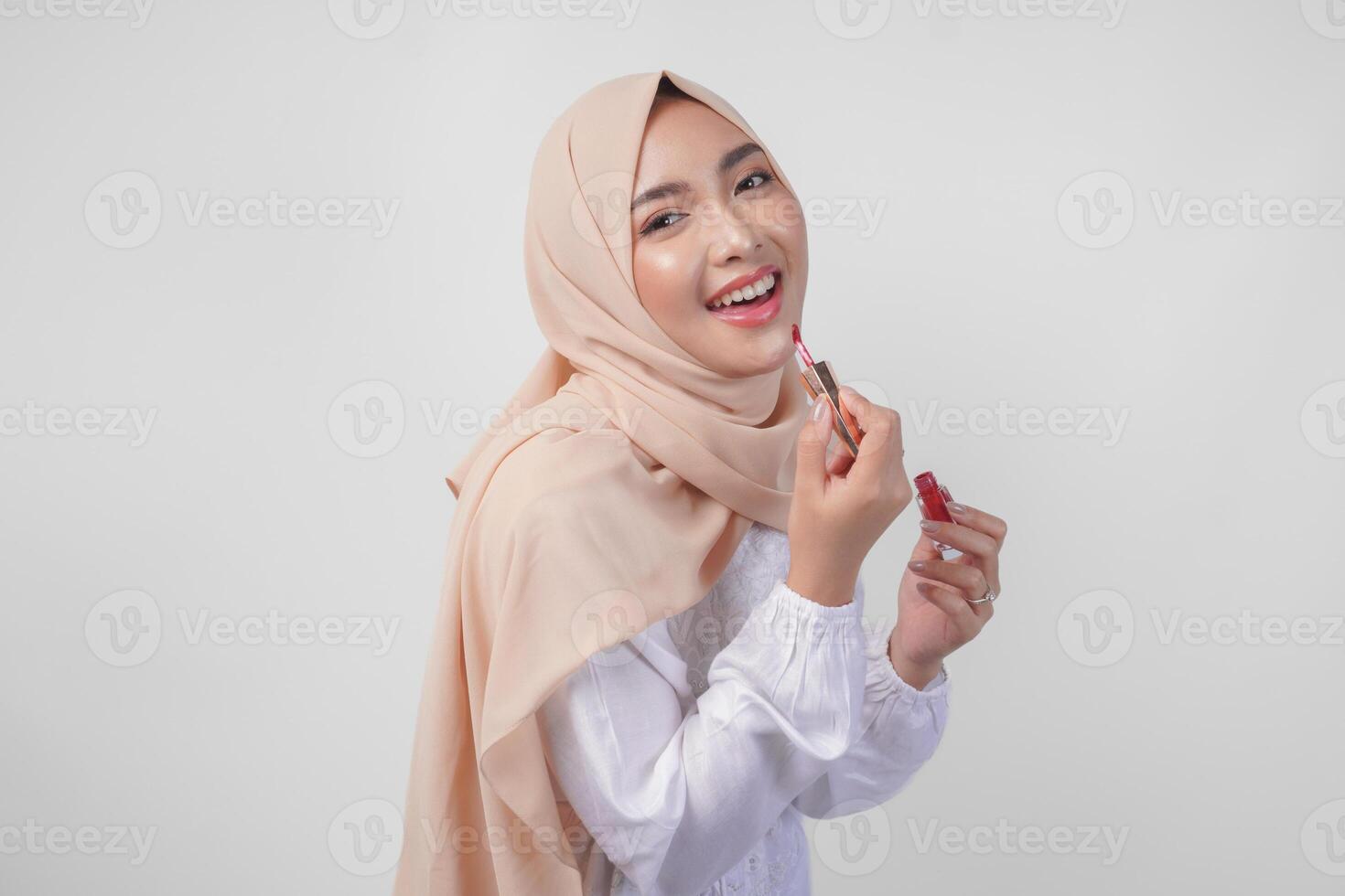 skön ung asiatisk muslim kvinna bär vit klänning och hijab sätta på smink applicering läppstift. mode och kosmetika skönhet begrepp foto