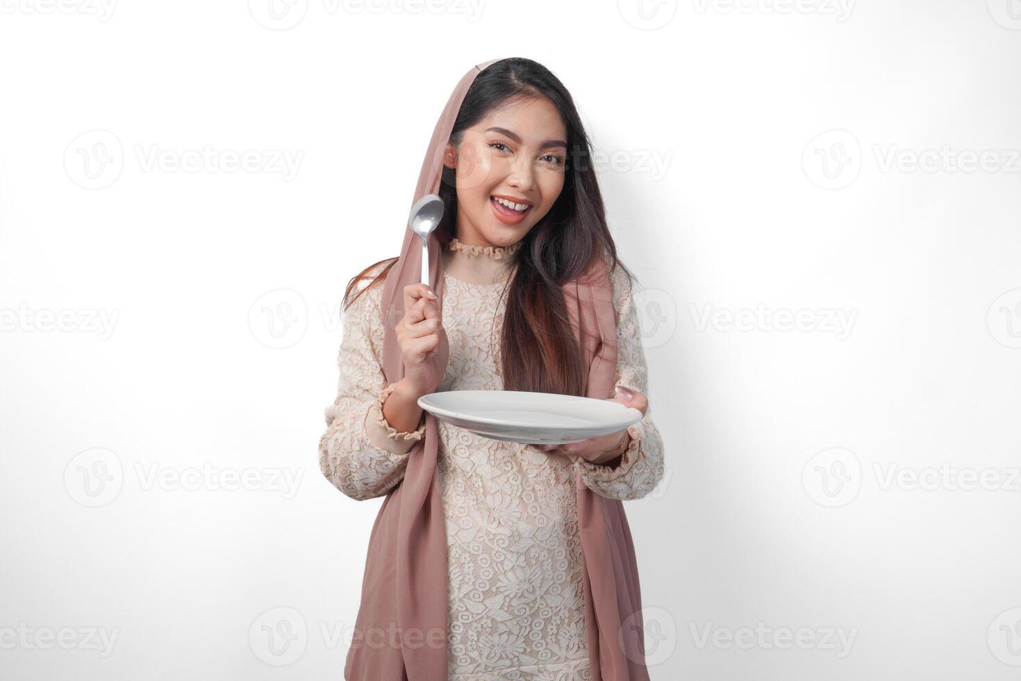 upphetsad asiatisk muslim kvinna innehav tallrik och bestick till äta efter fasta medan leende glatt på isolerat vit bakgrund. ramadan begrepp foto