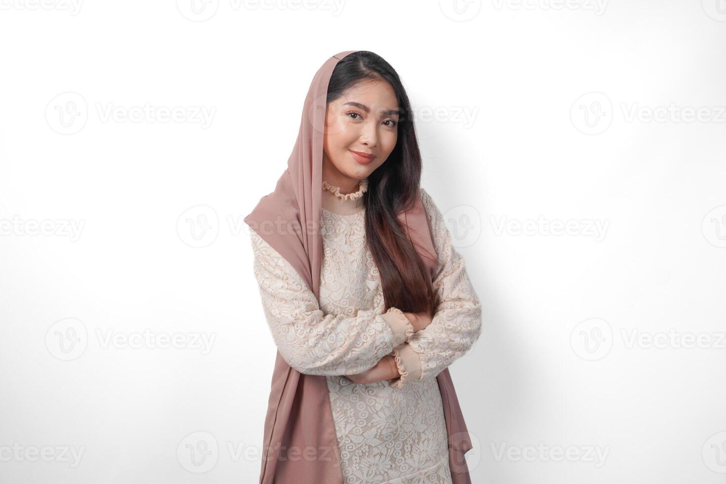 ung asiatisk muslim kvinna bär slöja slöja leende till de kamera med korsade vapen utgör full av förtroende, isolerat förbi vit bakgrund foto