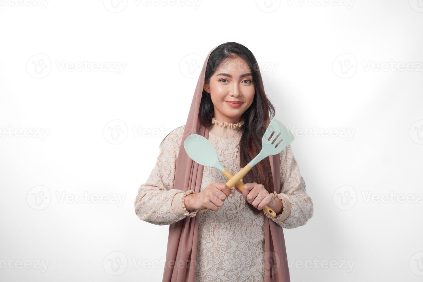 skön asiatisk kvinna i slöja hijab innehav matlagning redskap och framställning en vägran eller avslag tecken, ordspråk Nej, be till sluta, stående över isolerat vit bakgrund foto