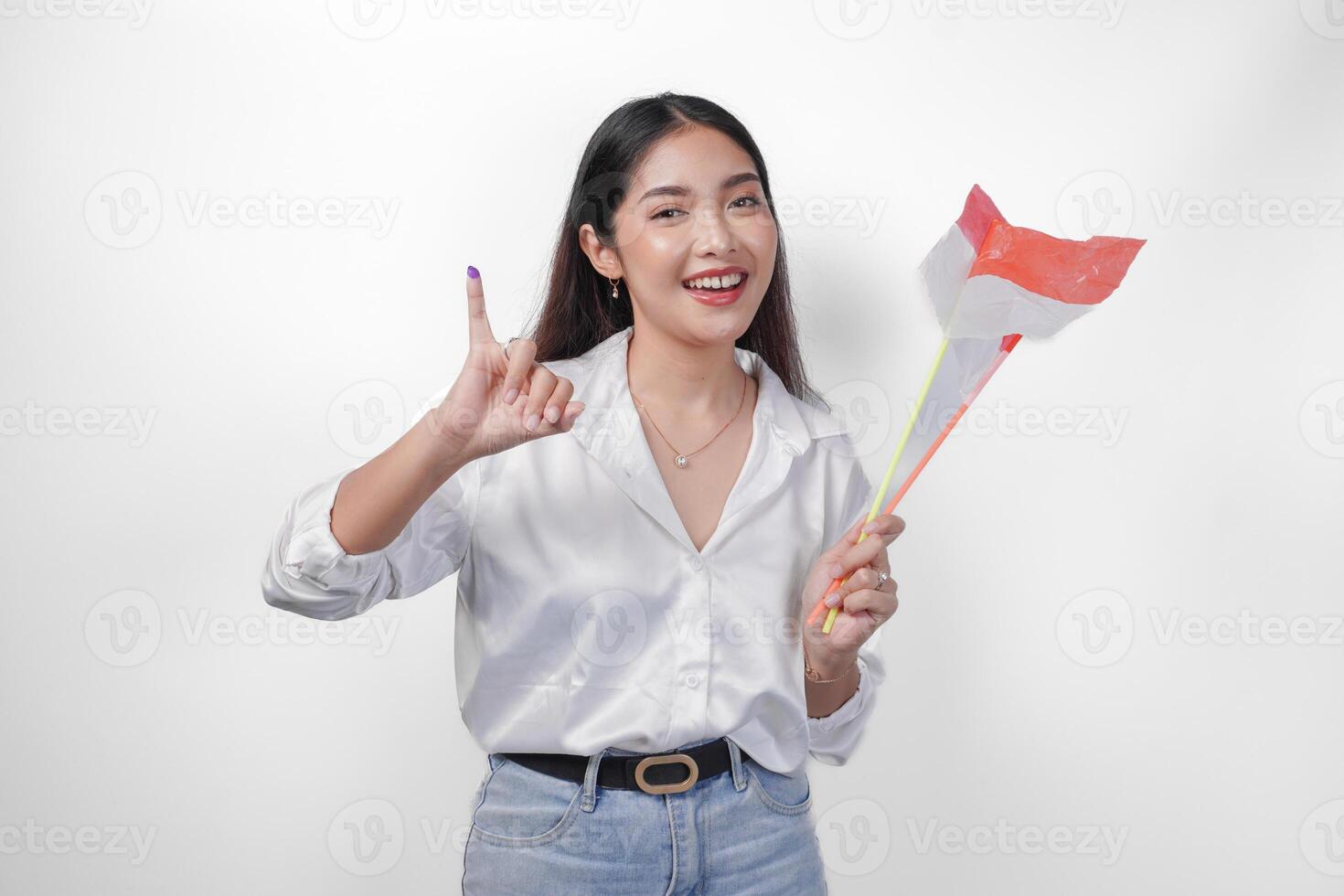 porträtt av Lycklig asiatisk kvinna stolt som visar liten finger doppade i lila bläck efter röstning för president och parlament val, vänster hand innehav indonesien mini flaggor. oberoende dag begrepp. foto