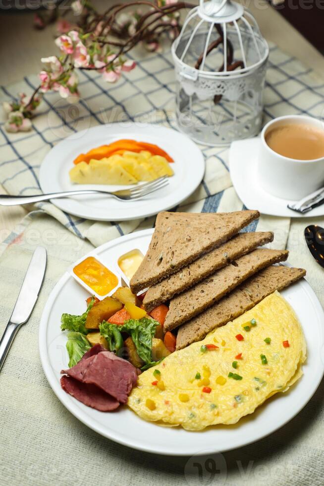 fylld omelett med bown bröd, kött, vegetabiliska sallad inkludera tomat, potatis, sallad blad och morot med te, kaffe, och ljuv melon eras på mat tabell topp se friska frukost foto