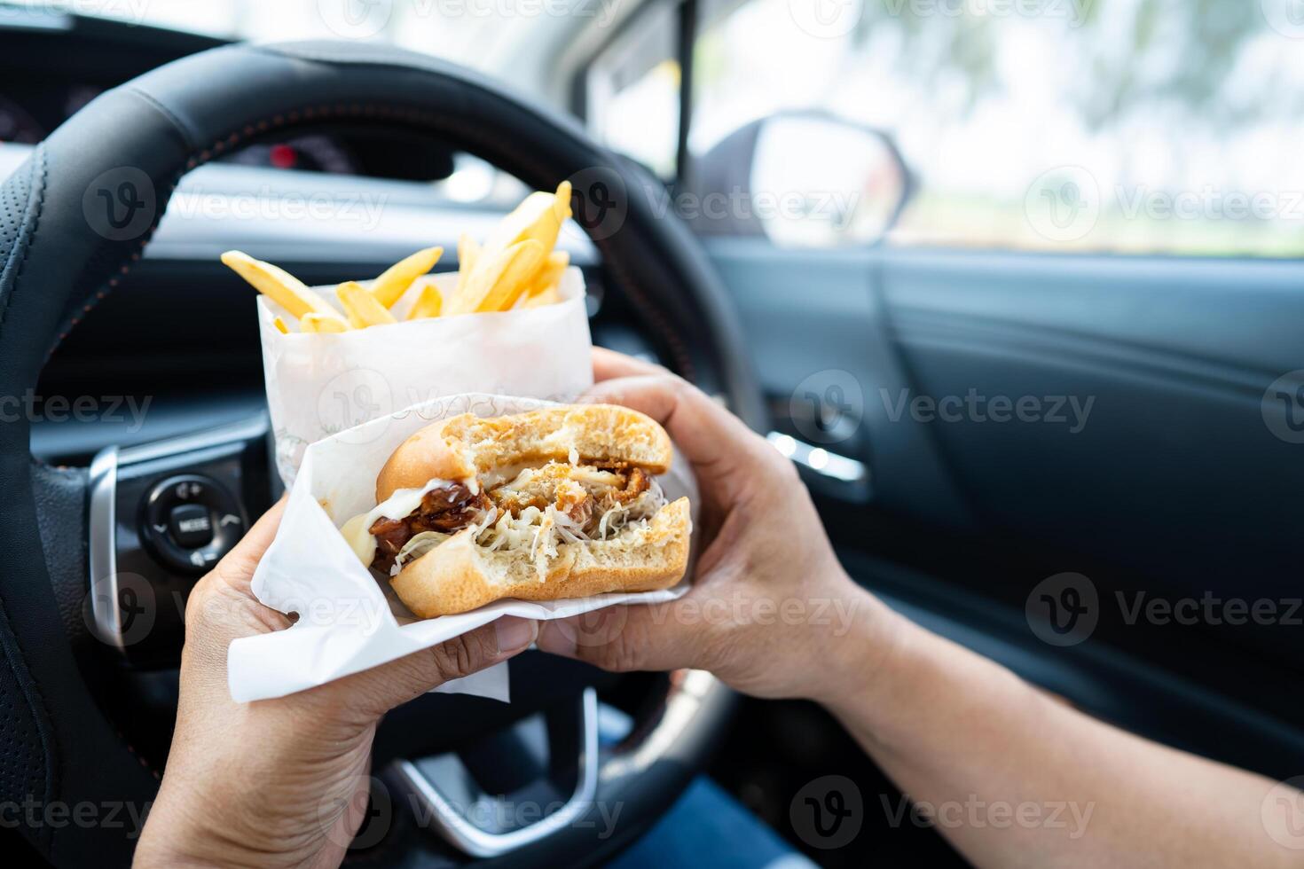 asiatisk lady innehav hamburgare och franska frites till äta i bil, farlig och risk ett olycka. foto