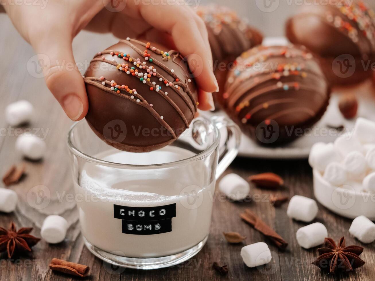 choklad kakao bomba i hand nära glas kopp med växtbaserad mjölk och choco bomba text. boll tillverkad från mjölk choklad med marshmallow. eleganta orange tonad bild av trendig vinter- varm choklad dryck foto