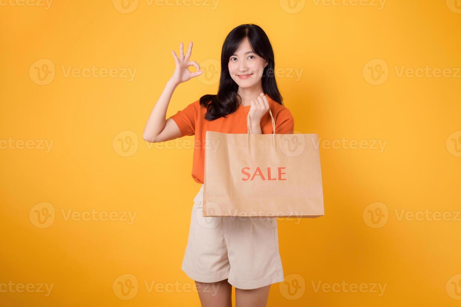 fira besparingar och stil i en handla spree. ung kvinna innehav en väska isolerat på gul bakgrund, strålande lycka i en köpcenter miljö. foto