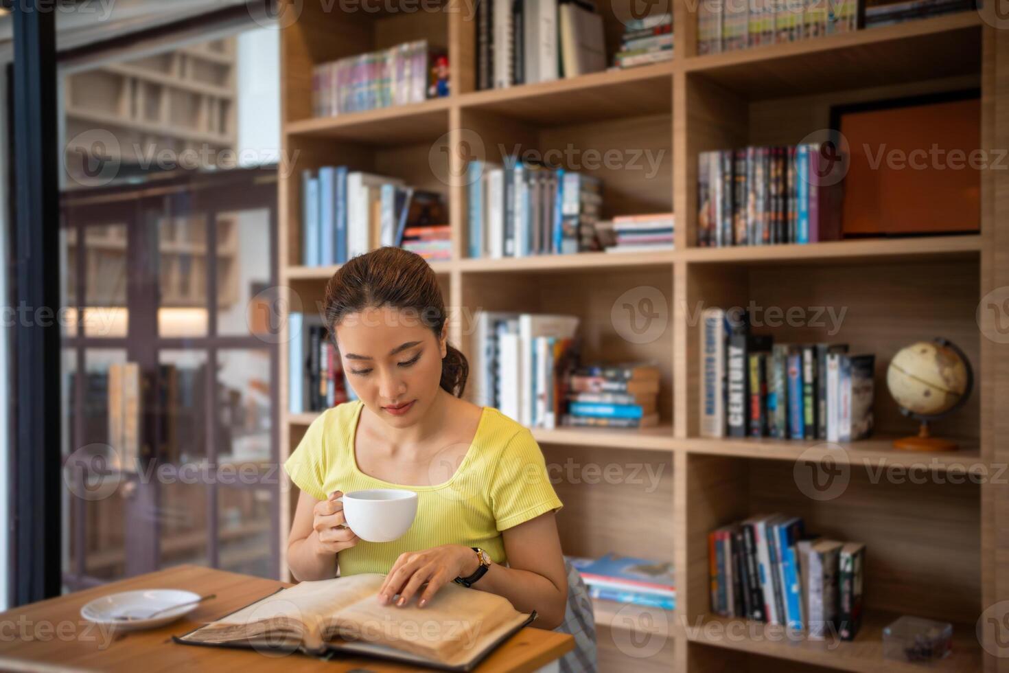 ung kvinna läsning bok och dryck varm kaffe i bibliotek på Hem, leende, skrattande, njuter bokmaskar hobby, Hem fritid tid foto