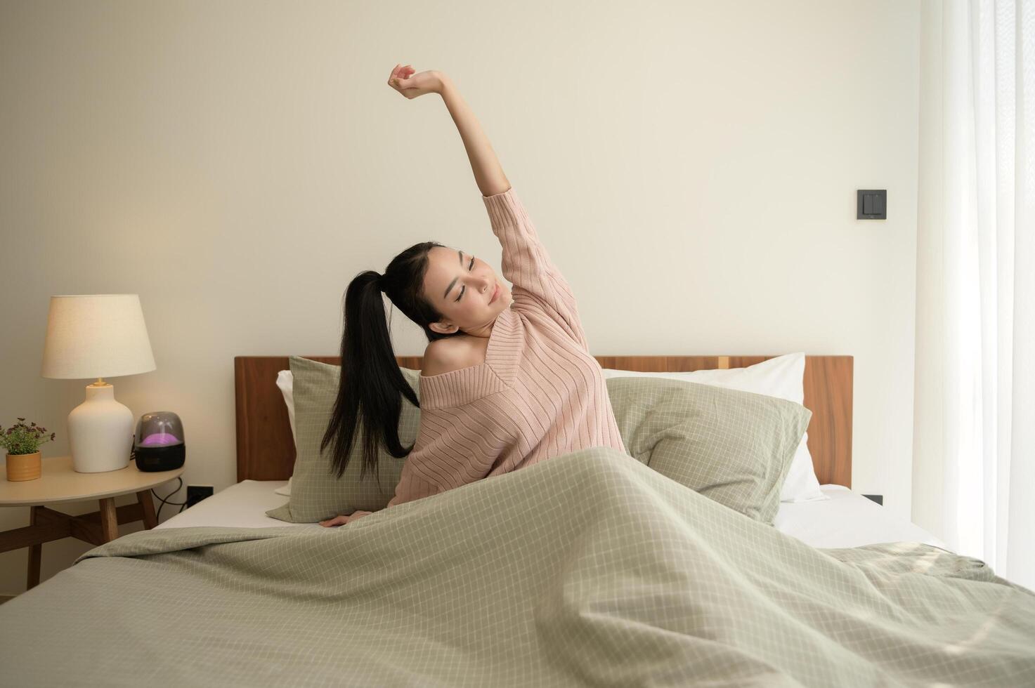 ung asiatisk kvinna stretching i säng efter vakna upp i de morgon- foto