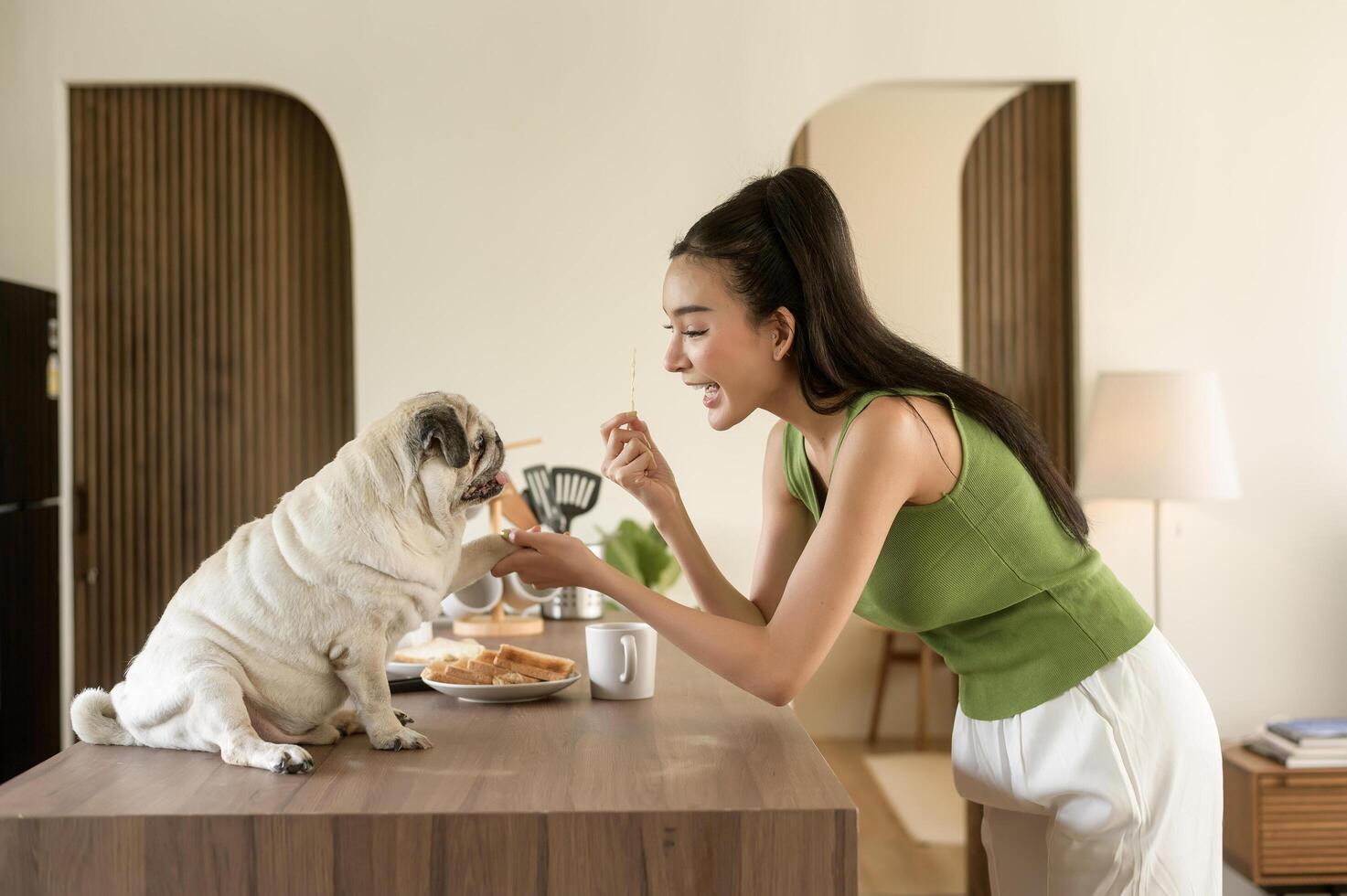 asiatisk kvinna framställning kaffe och rostat bröd bröd för frukost njut av med hund på de kök tabell i de morgon- foto