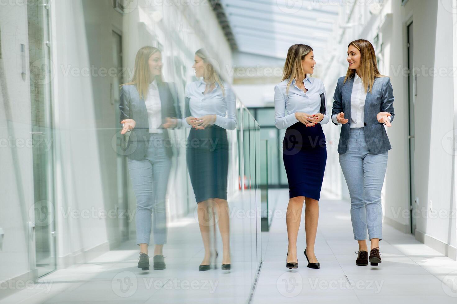 två ung företag kvinnor gående och diskuterar i de kontor hall foto