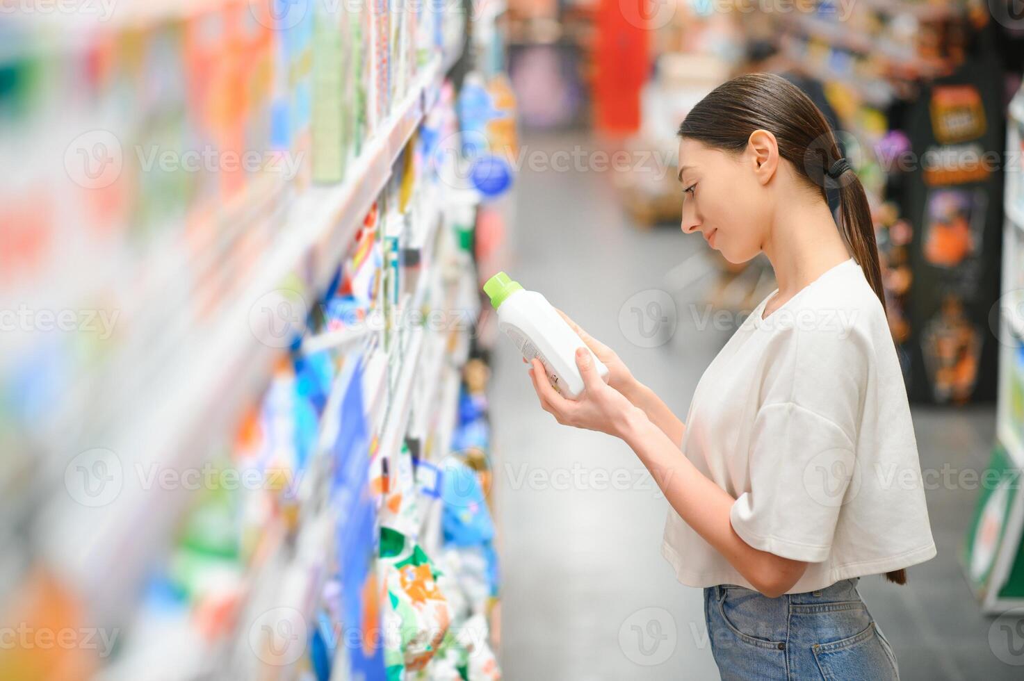 intresserad ung kvinna framställning inköp i hushåll kemikalier Lagra, läsning etiketter på flaskor foto