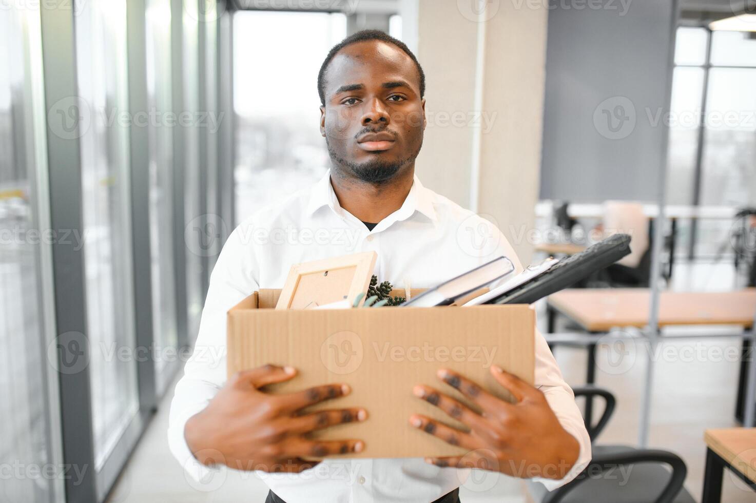 ung afrikansk man sparken innehav låda med personlig objekt på företag kontor foto
