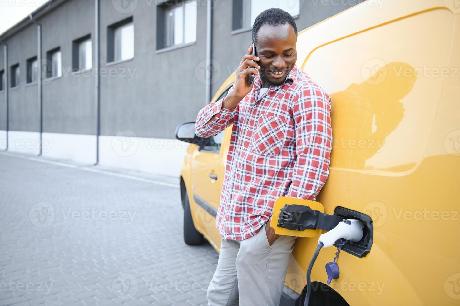 en afrikansk amerikan man står Nästa till gul elektrisk leverans skåpbil på elektrisk fordon laddning stationer foto